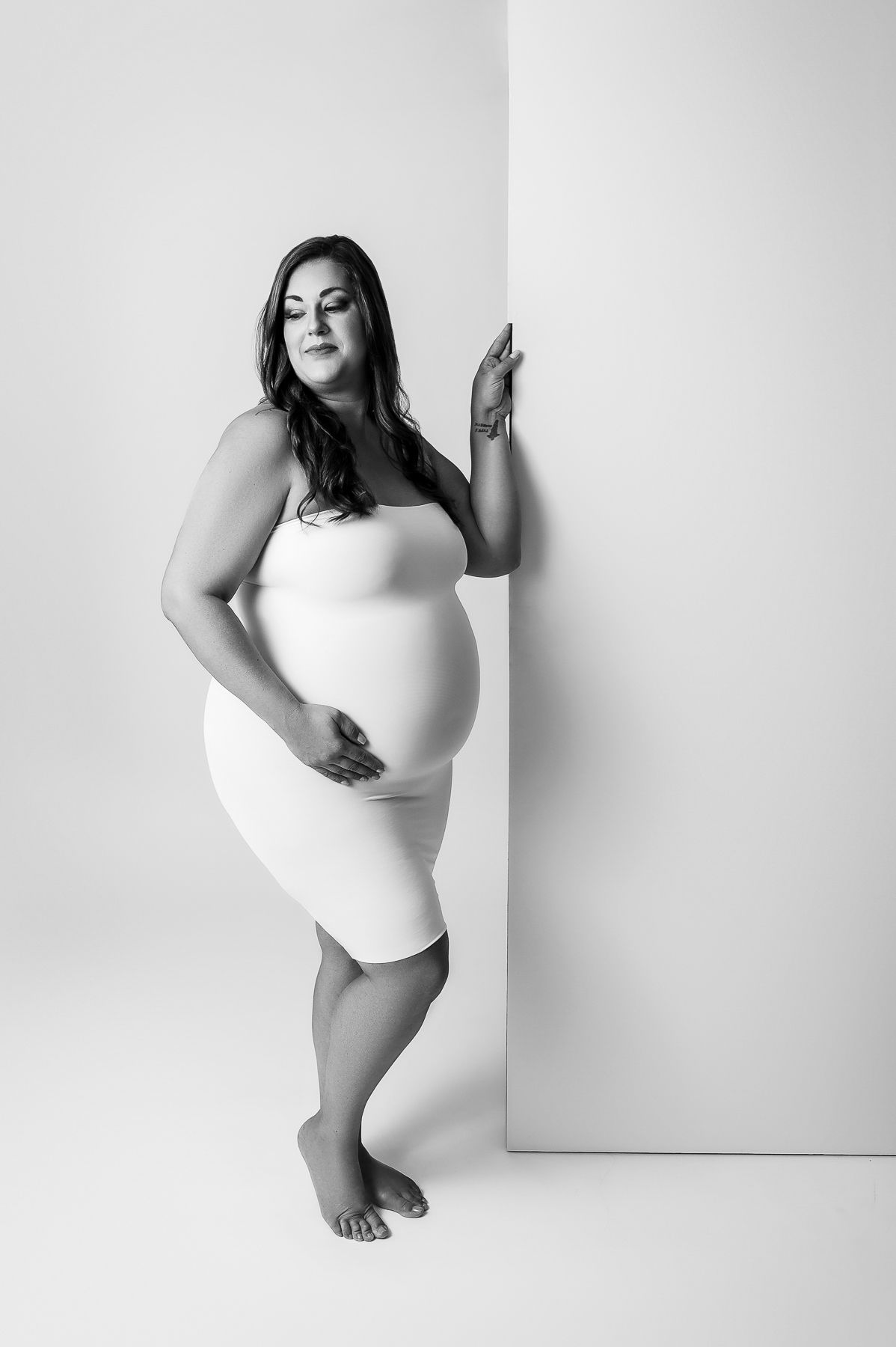 Artistic minimalist maternity photos in white bodysuit against white background.
