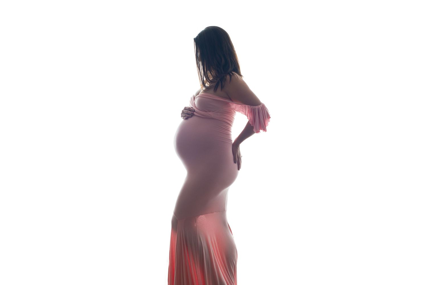 Artistic maternity photos in burgundy dress showing silhouette against white backdrop.