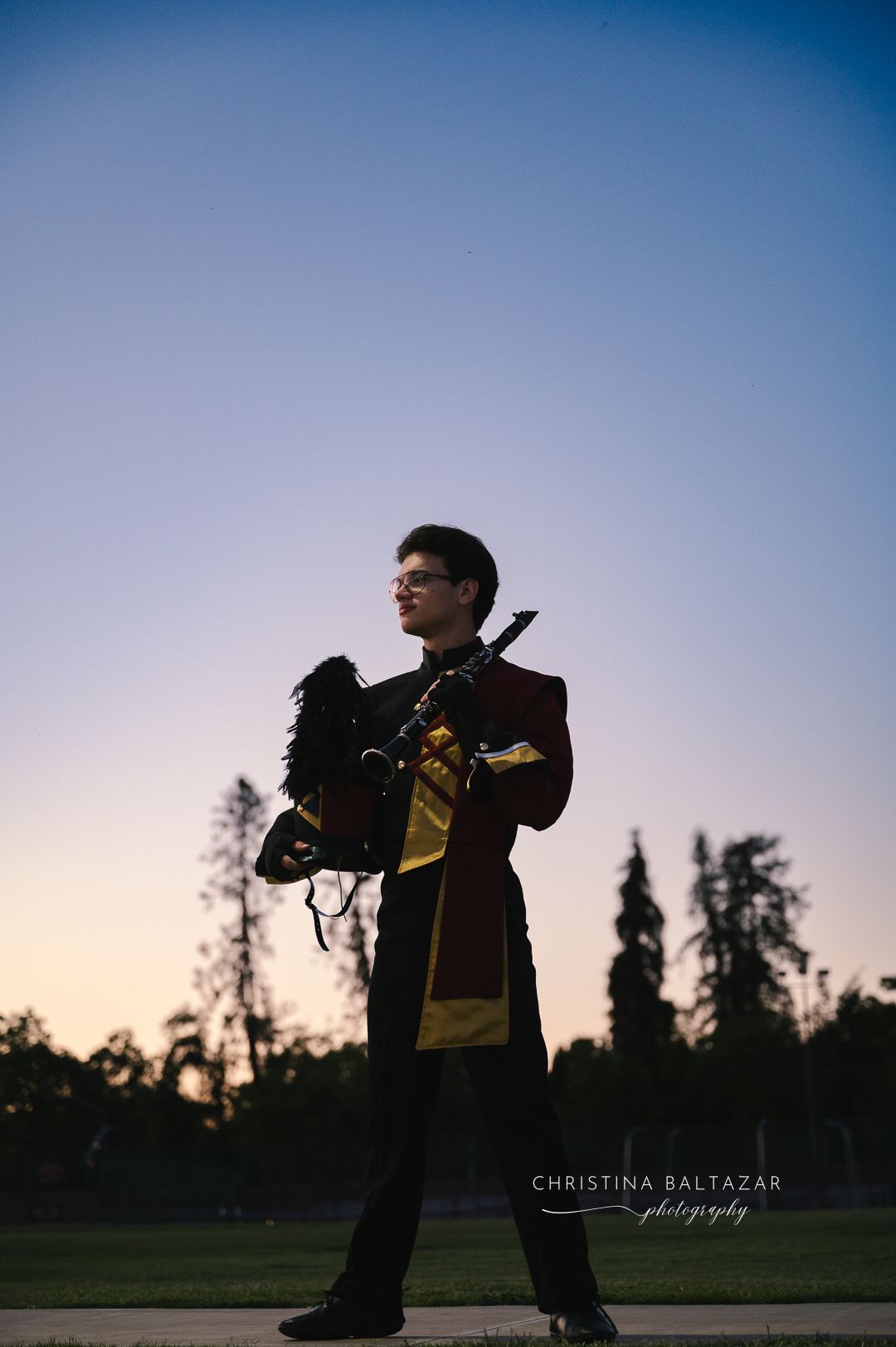 A silhouetted figure in military dress uniform stands against a dusky sky with tall trees in the background. Hanford Senior Photos