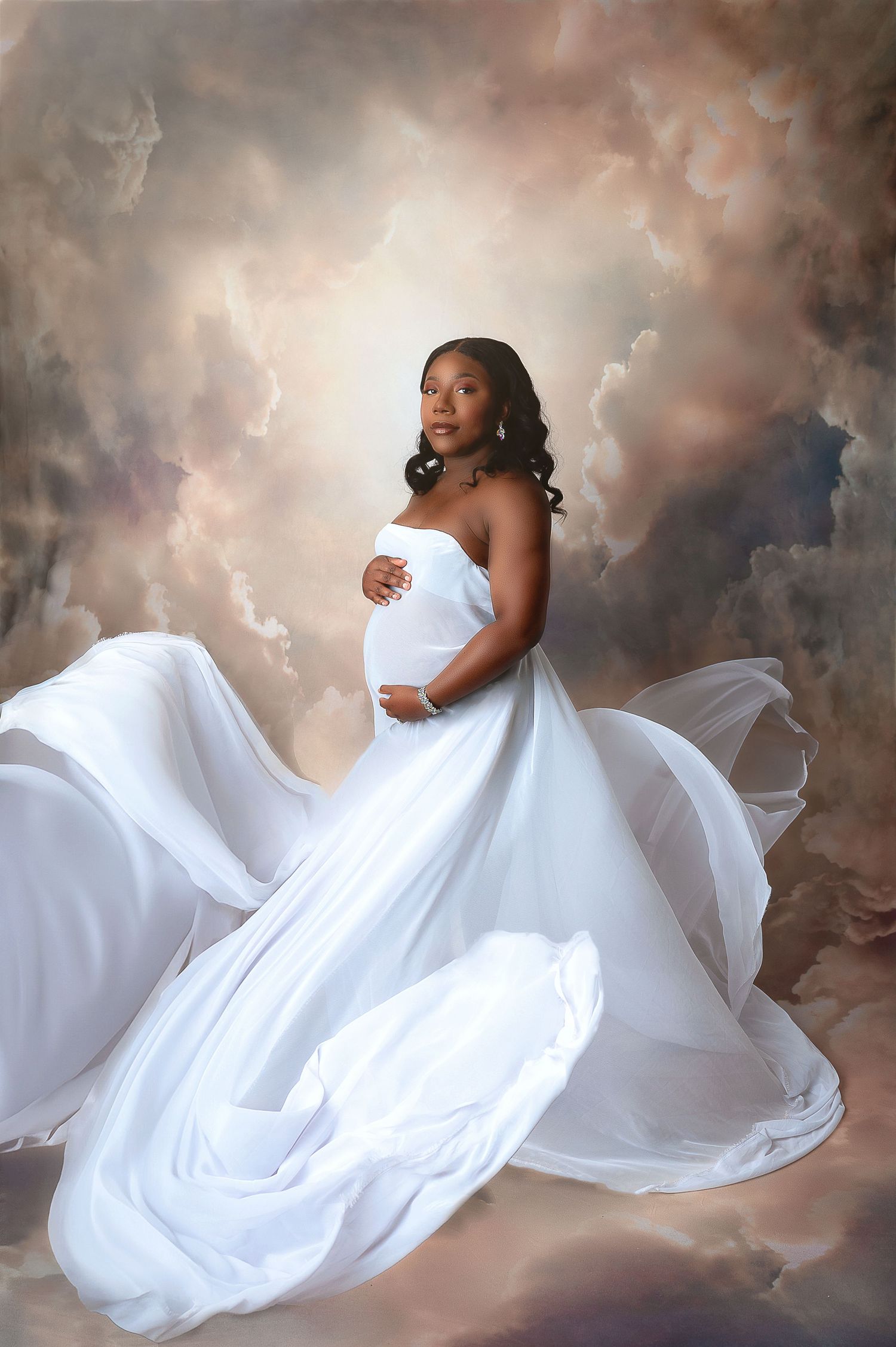 Elegant maternity portrait in flowing white gown with dramatic cloud background. Fresno Maternity Photographer