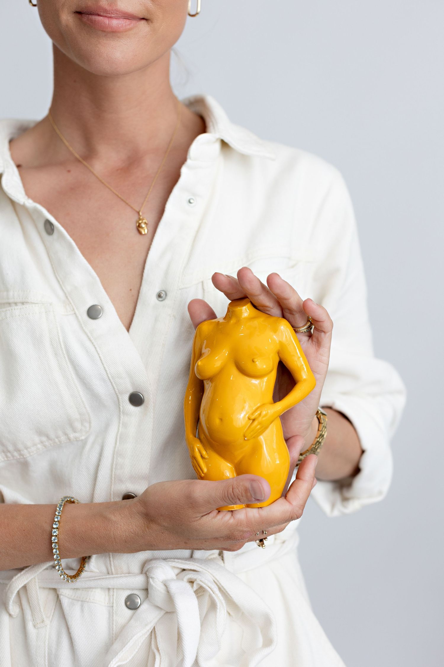 Woman in white shirt holding a yellow pregnancy sculpture against a light gray background.  3D Pregnancy Sculpture