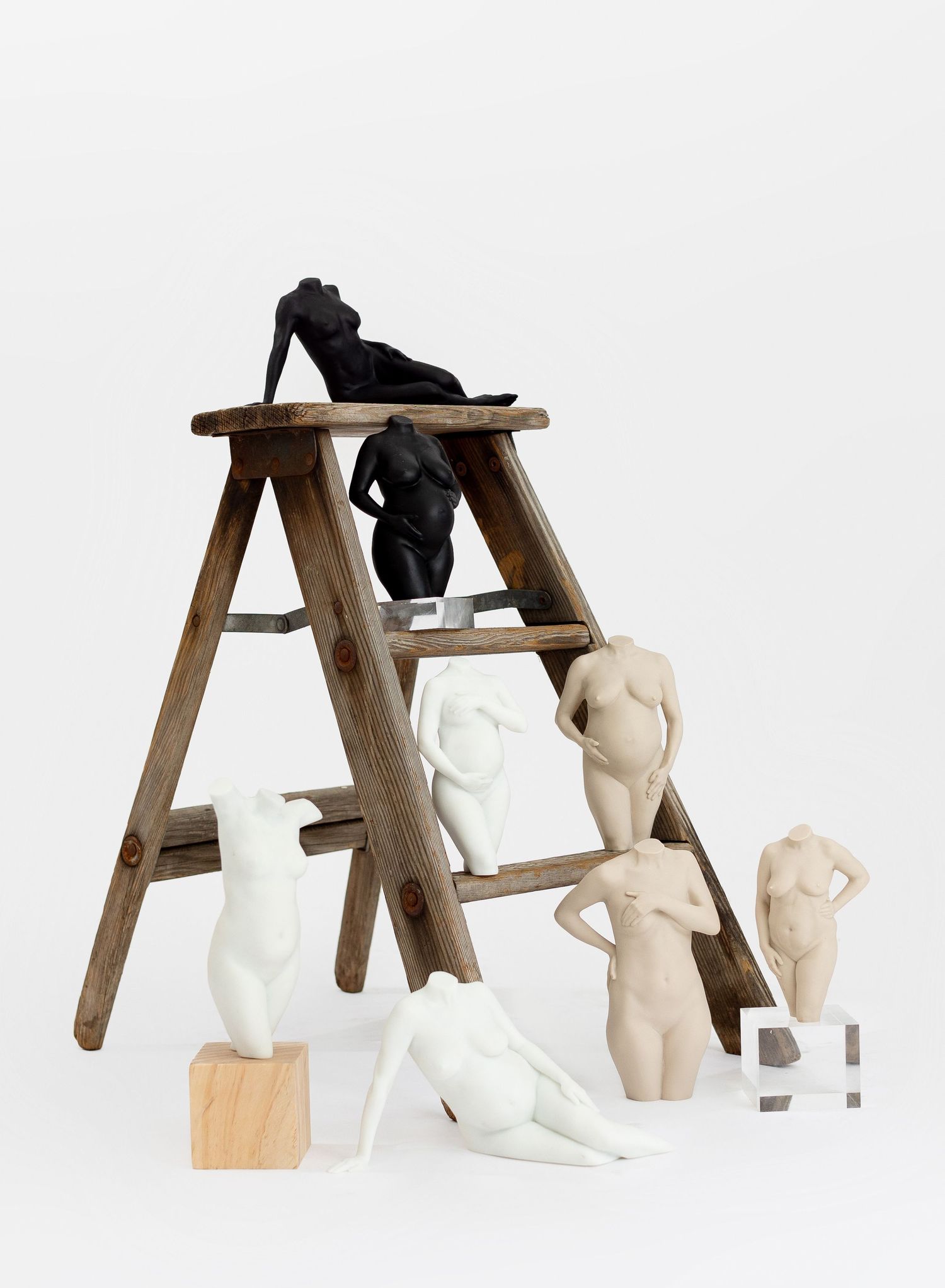 Collection of female pregnancy sculptures in black, white, and beige displayed on a rustic wooden ladder and pedestals in Lemoore, CA.