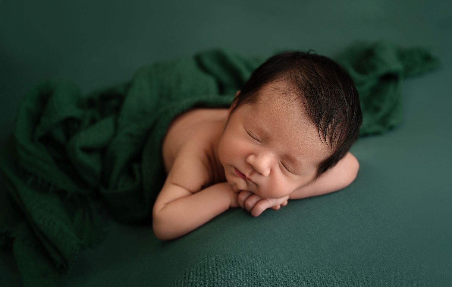Artistic newborn photography series on dark green velvet backdrop.