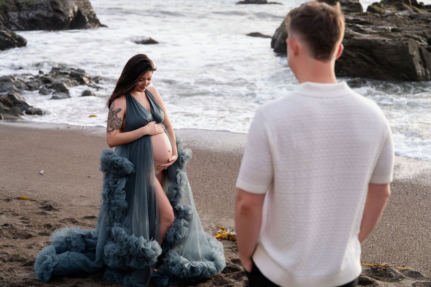 Maternity beach photoshoot with teal dress and crashing waves.