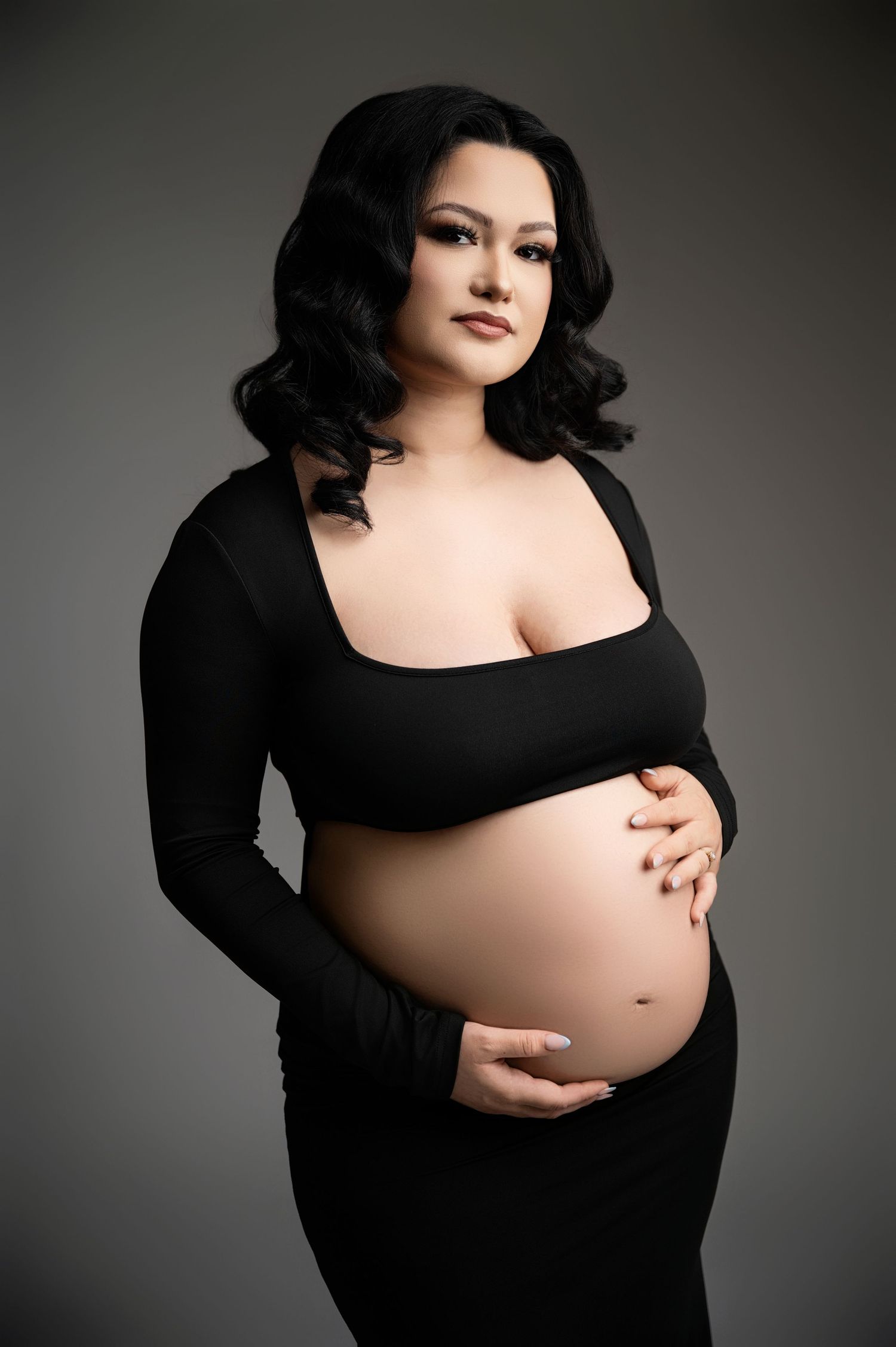 Dramatic black and white maternity photos showcase an elegant black dress against a dark background.