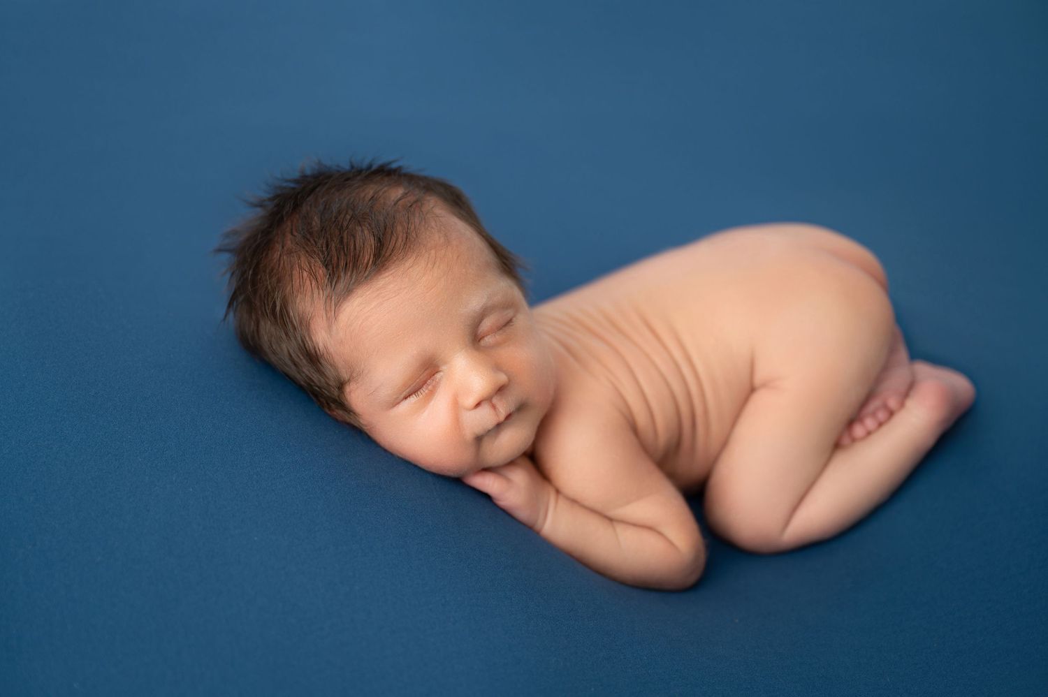 Newborn baby sleeping peacefully on blue backdrop in natural pose.