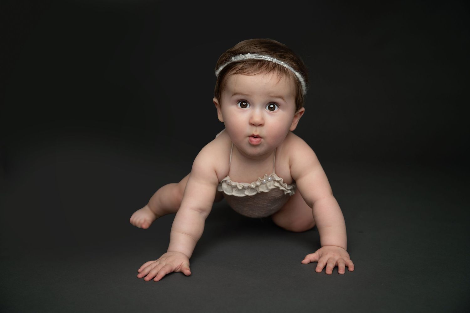 Professional baby portraits against dark background showing crawling milestone.