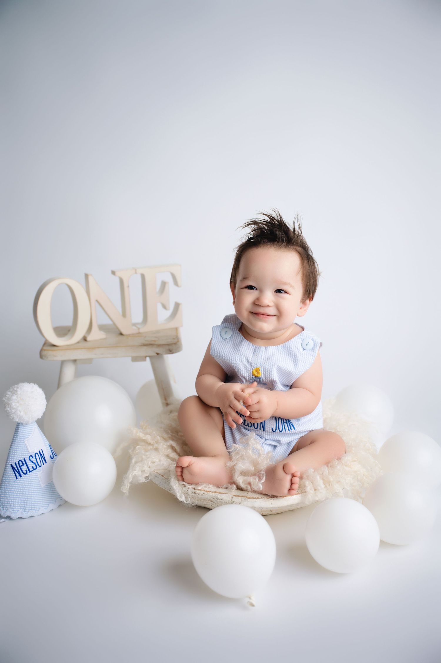 Baby photo session with white balloons and decorative elements on light backdrop.