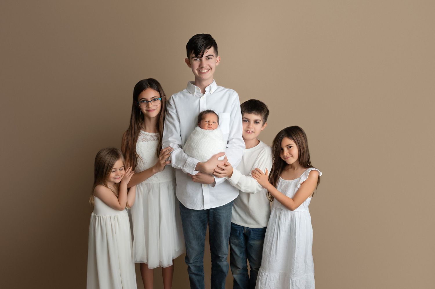Family portrait of siblings and parents in coordinated white outfits against neutral background.