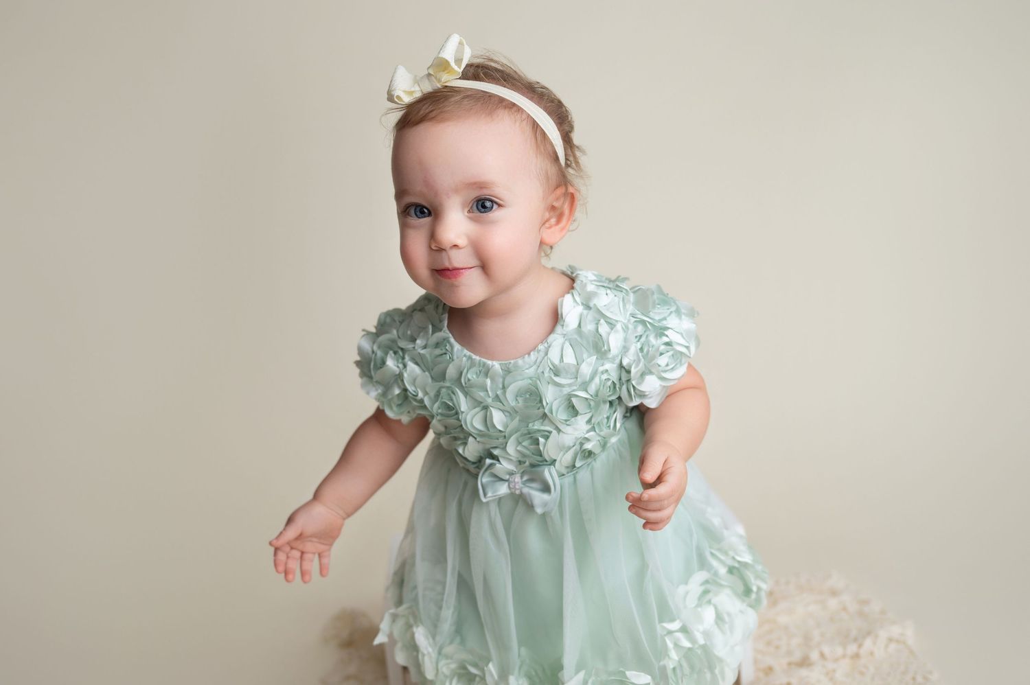 Baby wearing mint green dress smiles during professional photo shoot.