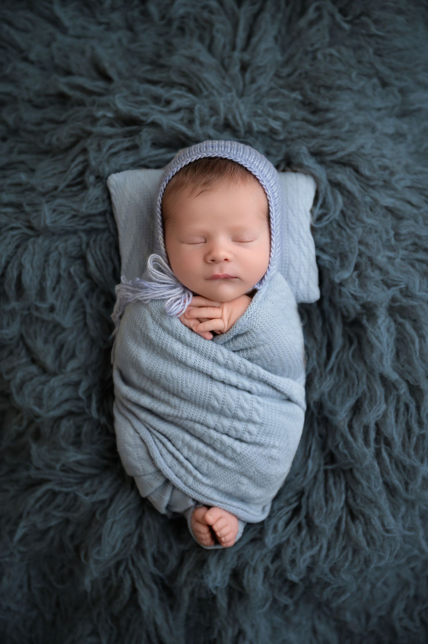 Peaceful sleeping newborn swaddled in soft blue bonnet and wrap on textured teal fur blanket.  Fresno Newborn Photographer
