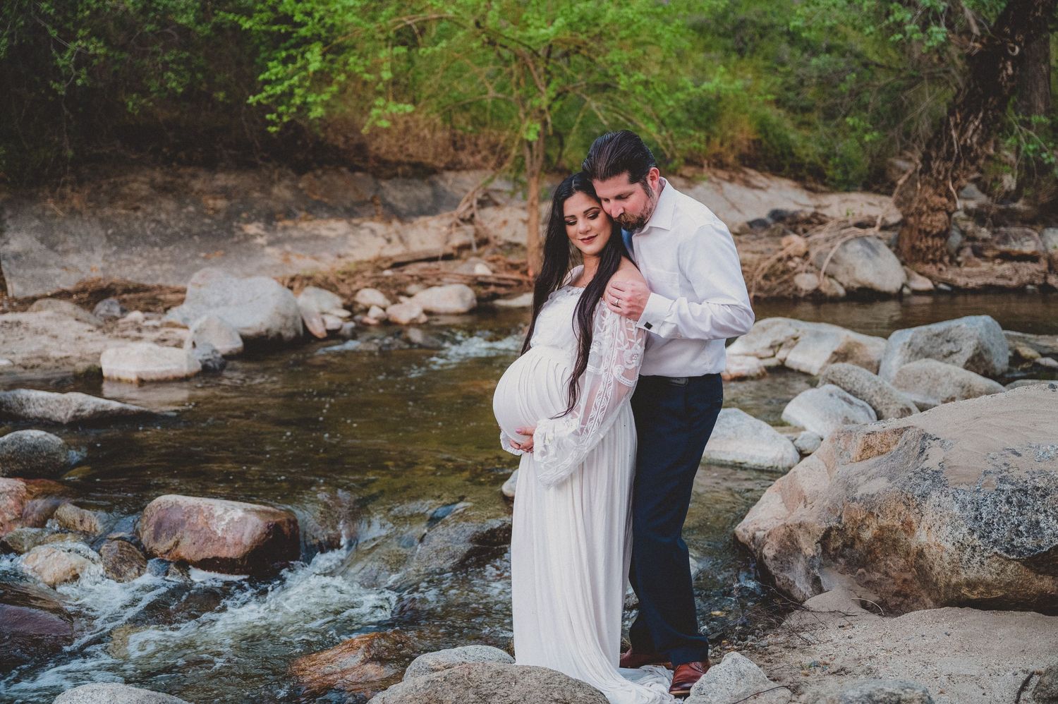 Couple shares intimate moment while standing on rocks beside flowing stream. Fresno Family Photography