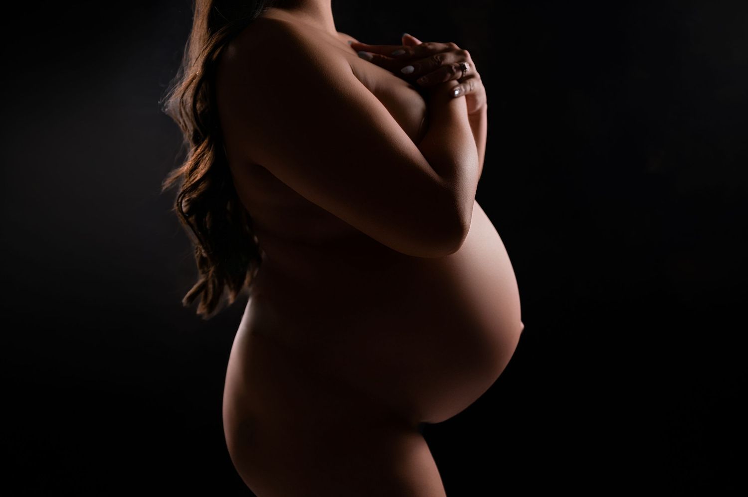 Artistic silhouette of a pregnant woman posing against a dark background, showcasing her baby bump.