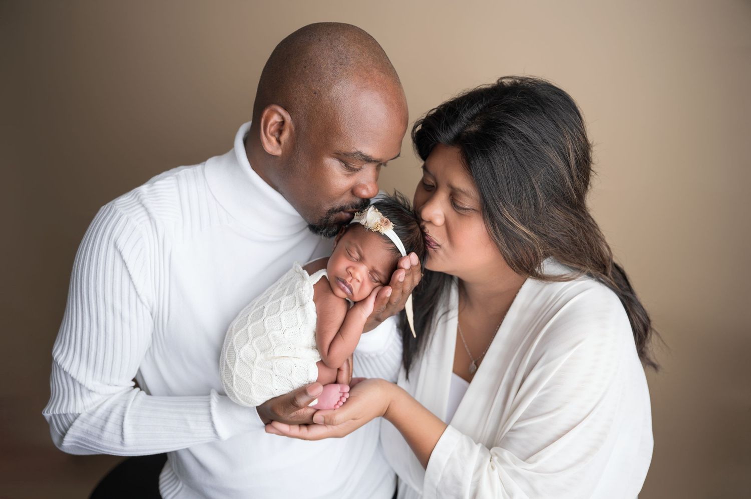 Parents tenderly hold and kiss their precious newborn baby against a neutral brown studio backdrop.  Fresno Newborn Photographer