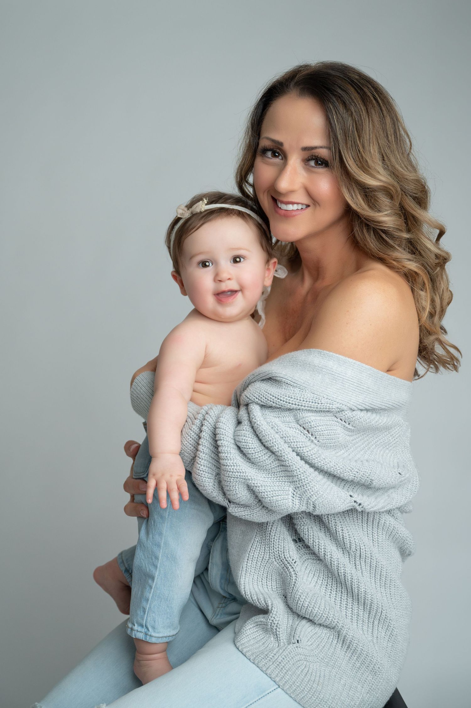 Mother and baby in coordinating gray and blue outfits pose during studio photo session.