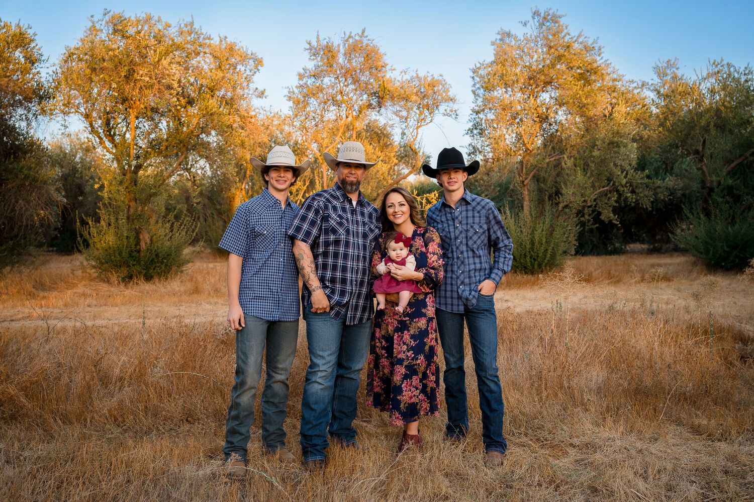 A group in western attire poses together against a backdrop of golden autumn trees at sunset.