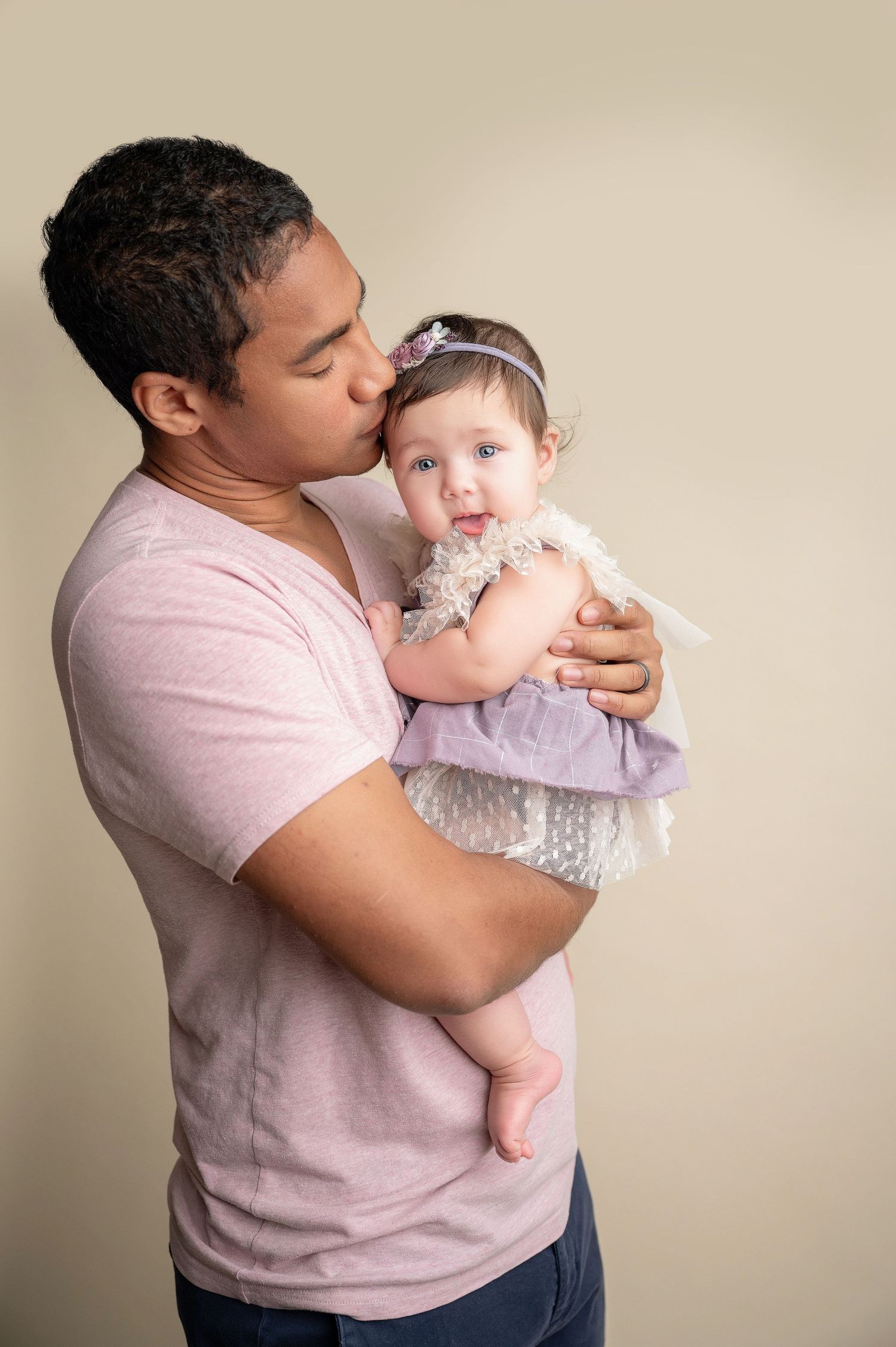 A tender moment between parent and baby in a studio portrait against beige background.