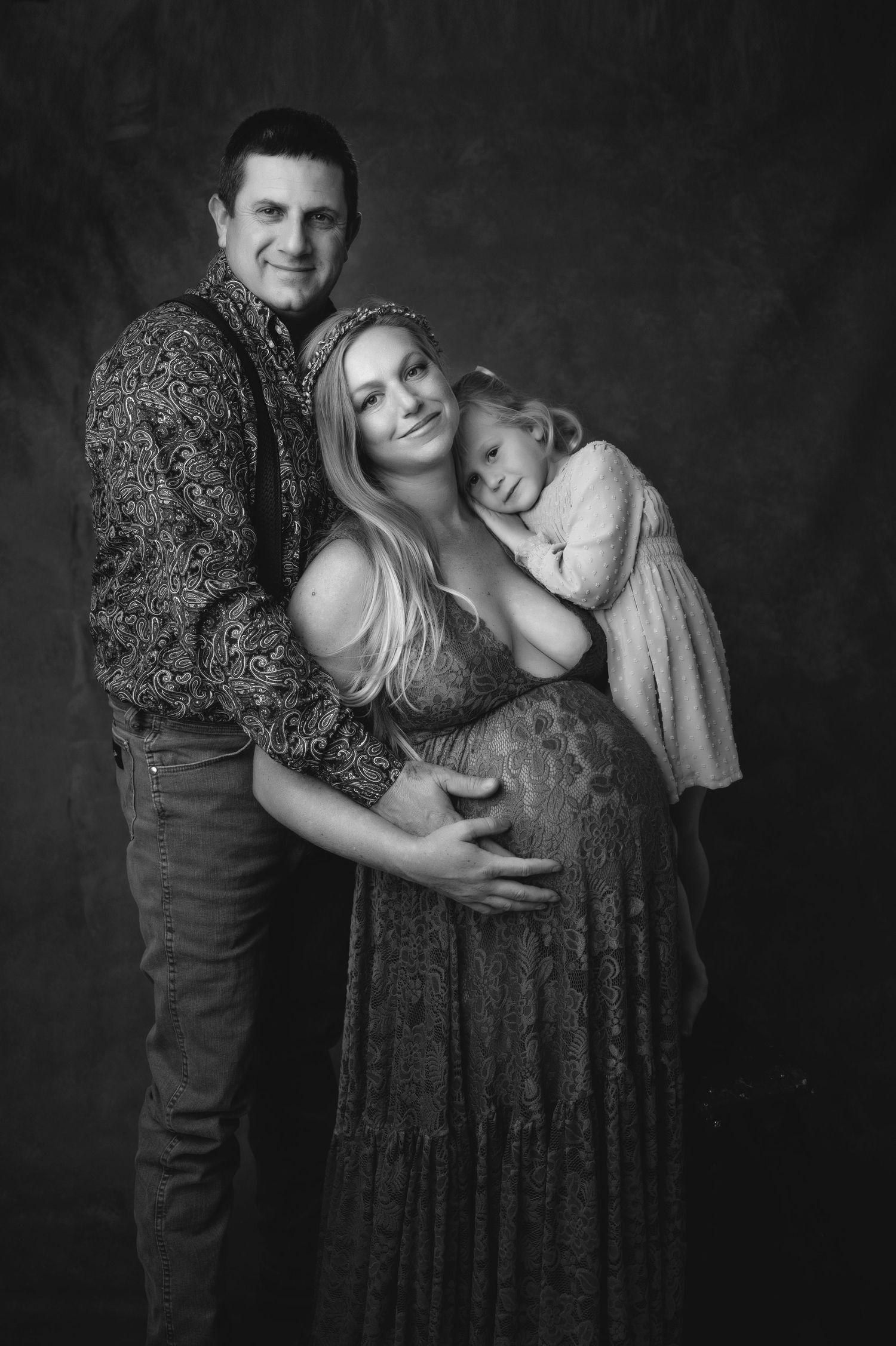 Black and white family maternity portrait with sparkly dress against dark backdrop.