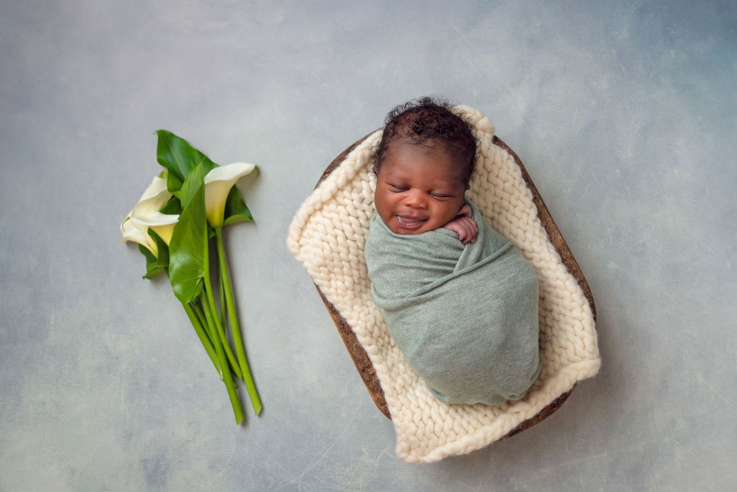 Newborn photography setup with white flowers and woven basket.
