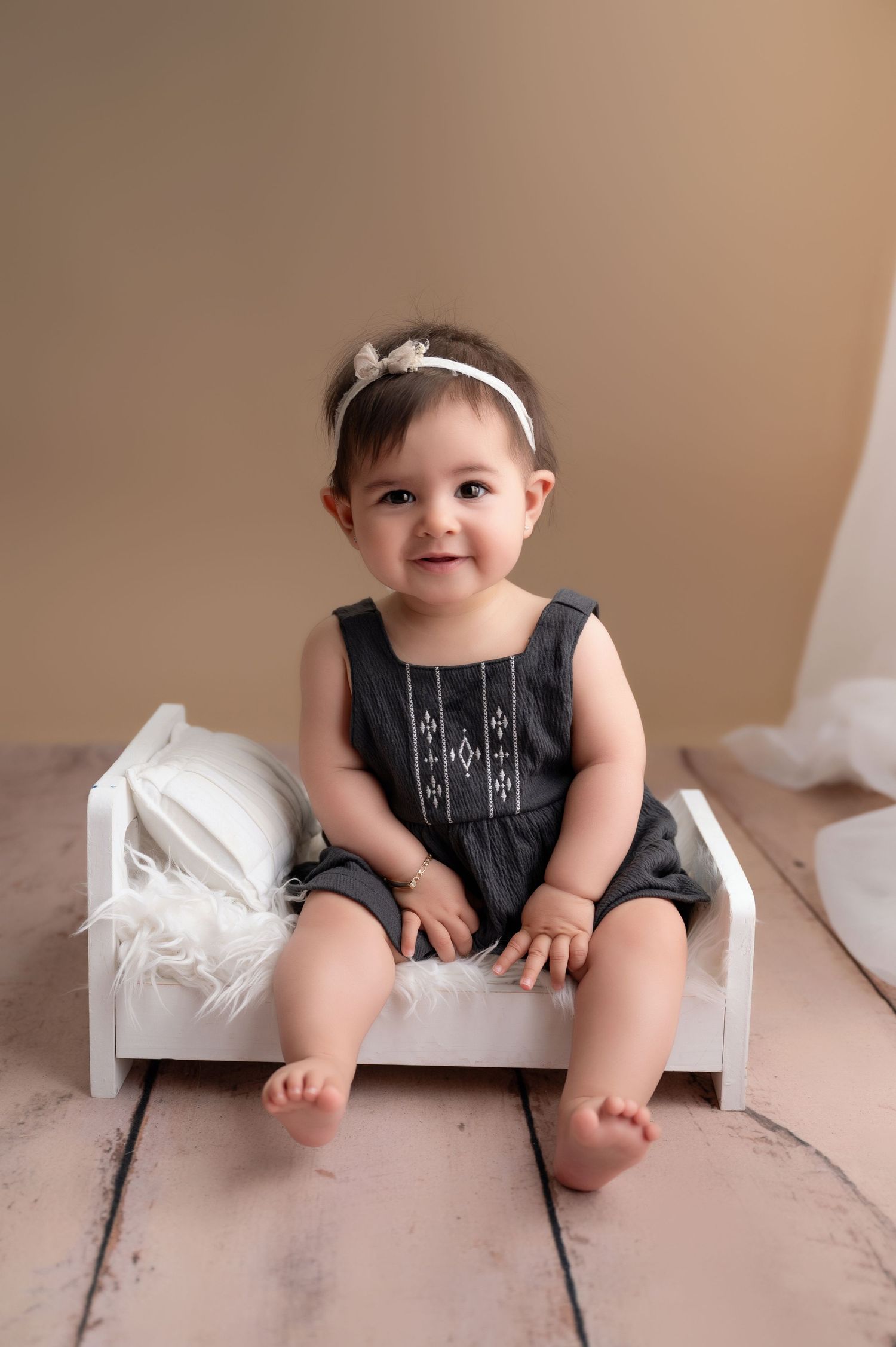 Baby in black romper sitting on white miniature bench showing developmental progress.