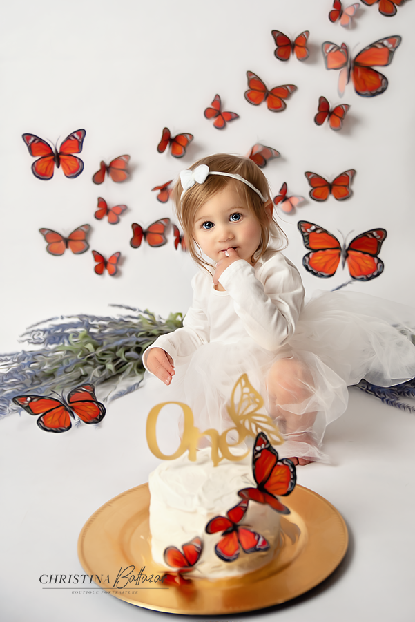Cake smash photo session with orange butterflies and gold accents on white background. Hanford Cake Smash Photos