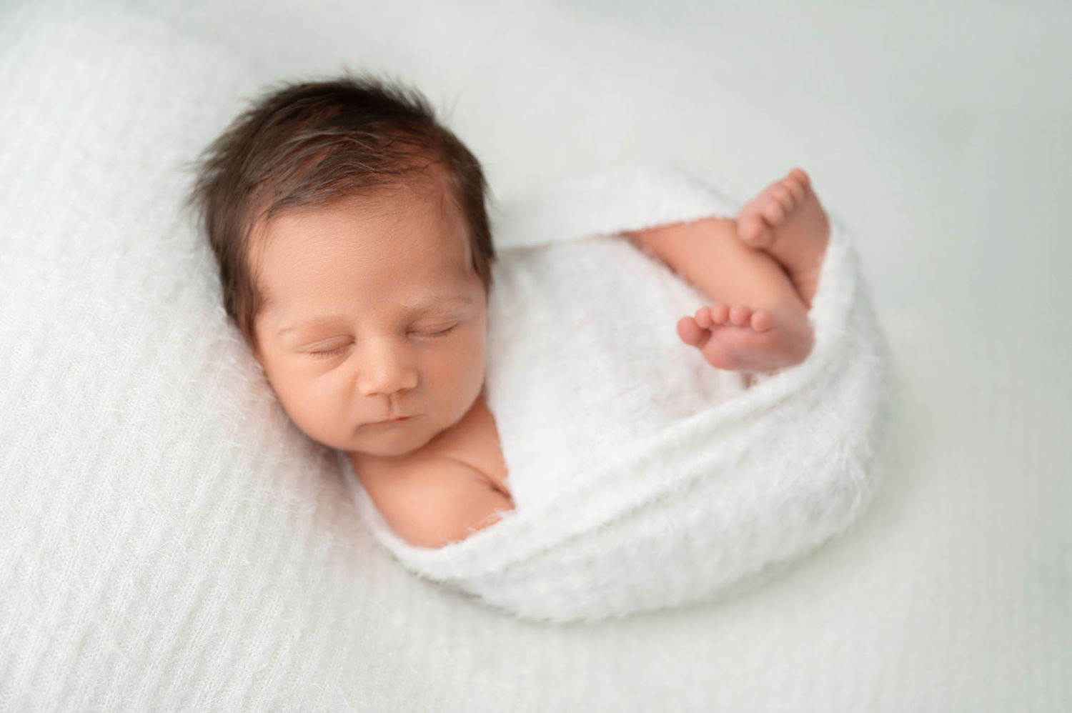 Peaceful sleeping newborn wrapped in white blanket during portrait session.