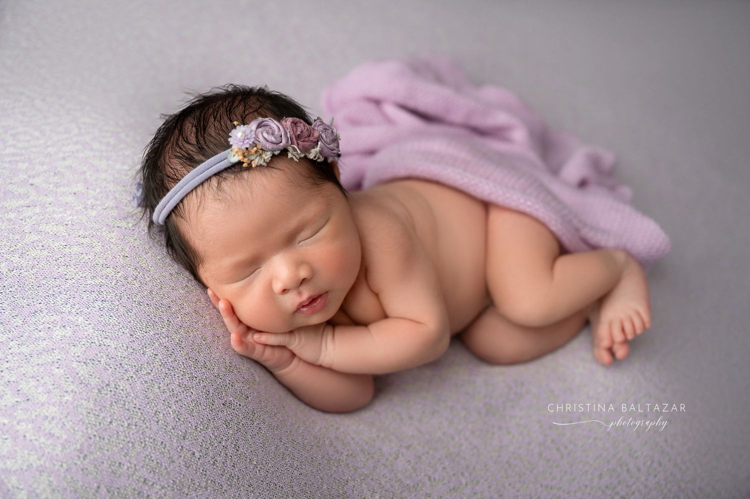 Sleeping newborn baby wearing delicate headband posed on soft gray blanket with pink fabric wrap. Fresno Newborn Photographer