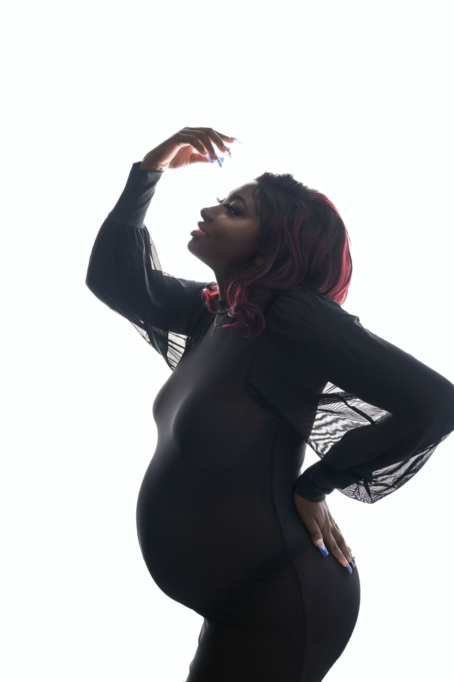 Silhouette of pregnant woman in black dress striking an artistic pose.