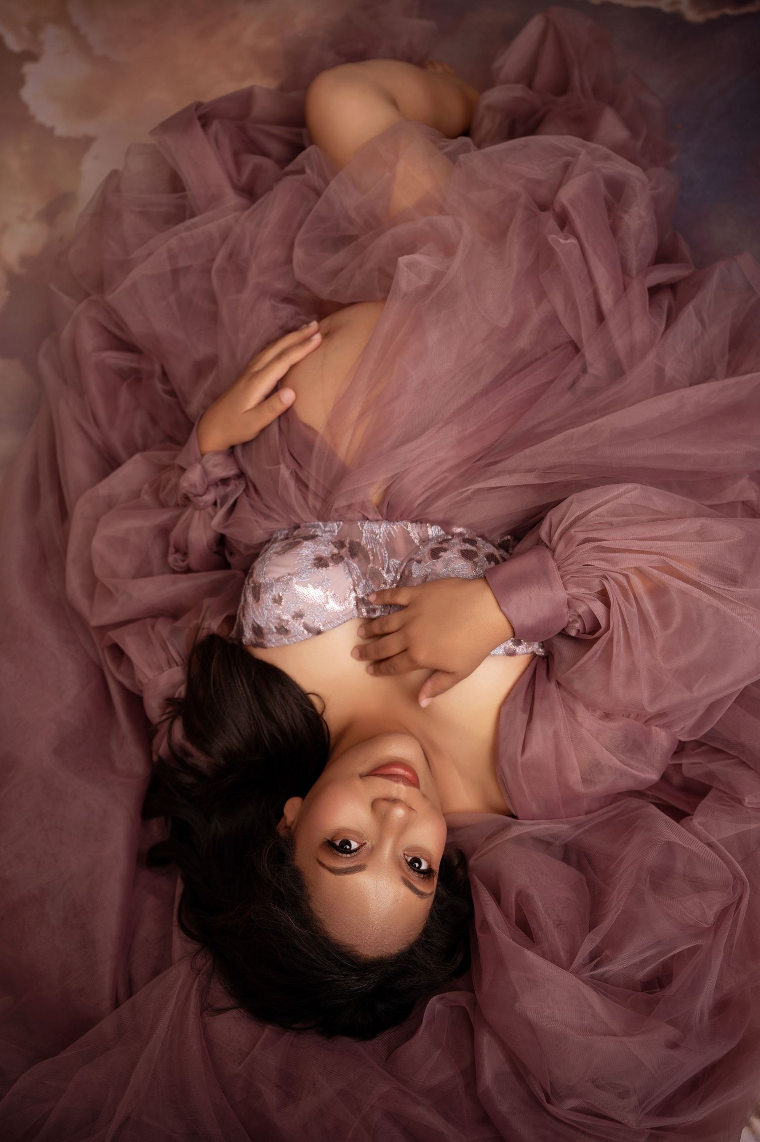 Romantic boudoir photo with flowing mauve tulle fabric creating dreamy ethereal atmosphere.