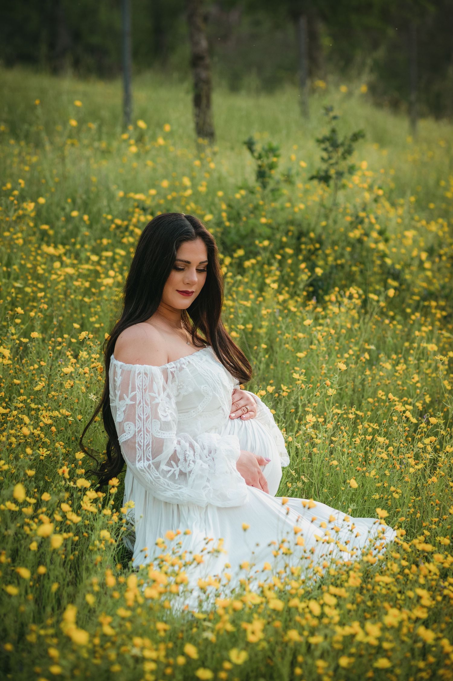 Expectant mother in white lace dress sits among yellow wildflowers. Hanford Maternity Family Photographer