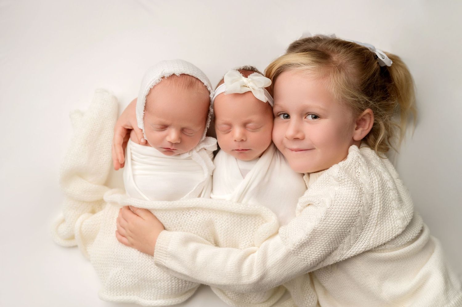 Sweet portrait series of siblings in cream sweaters cuddling with newborn babies.