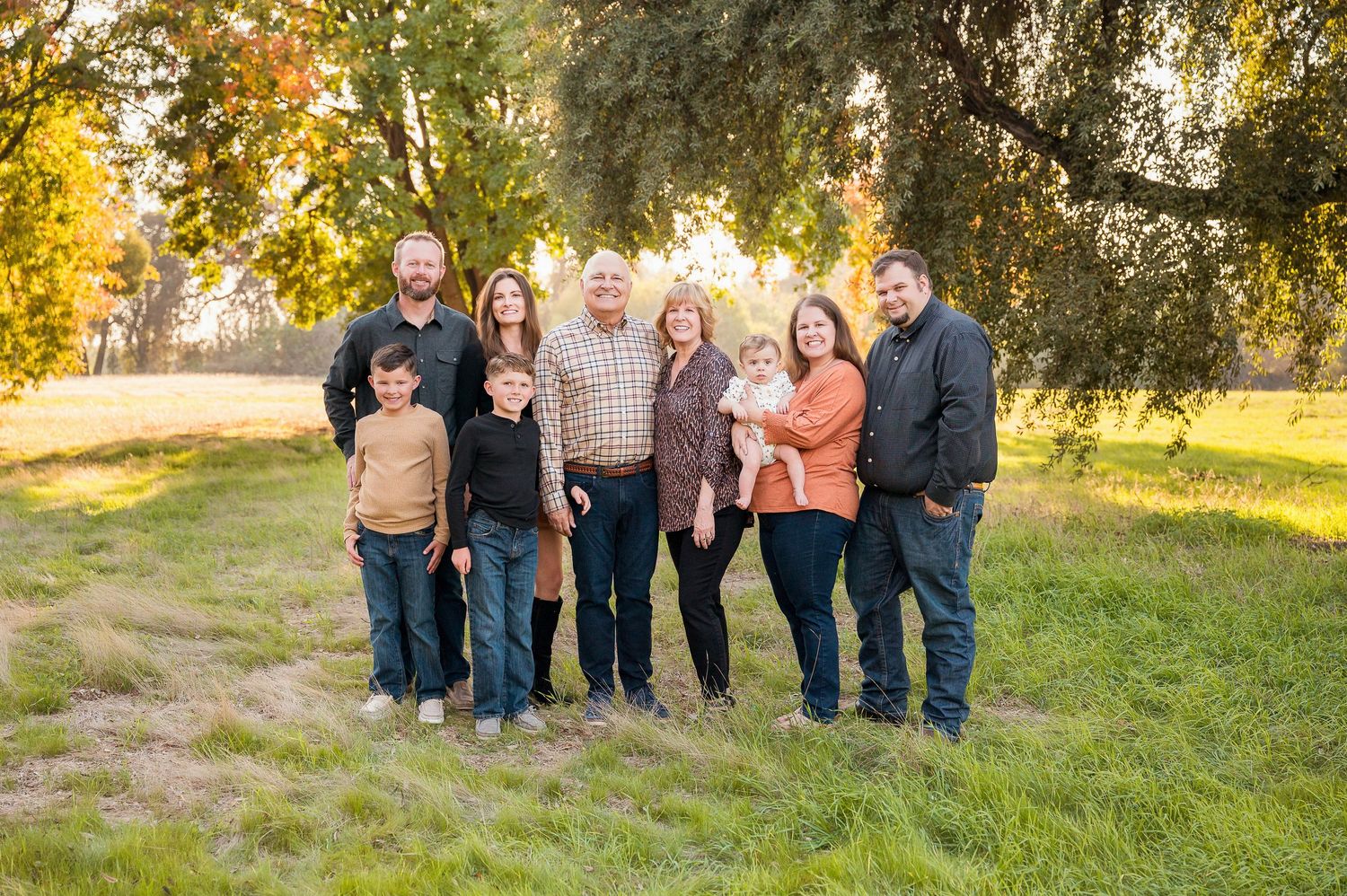 Extended family poses together on grassy hill during golden hour autumn photoshoot. Hanford Family Photographer