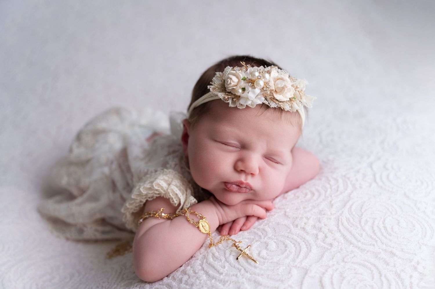 Peaceful newborn baby sleeping on white textured blanket wearing delicate crown.