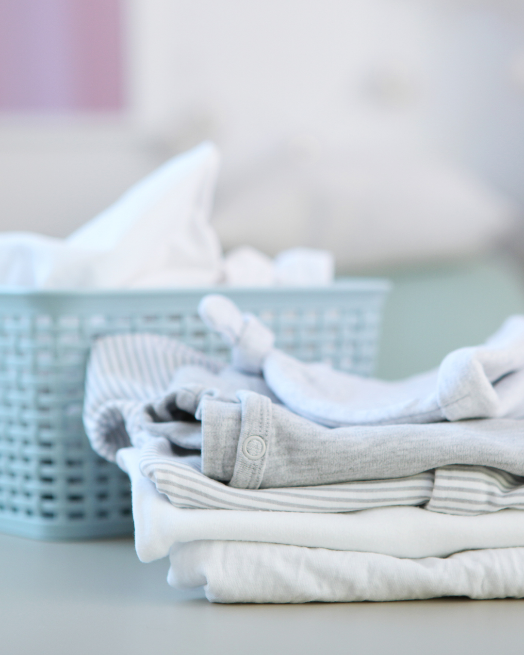 Neatly folded white and gray clothing items stacked beside a mint green storage basket on a clean surface.