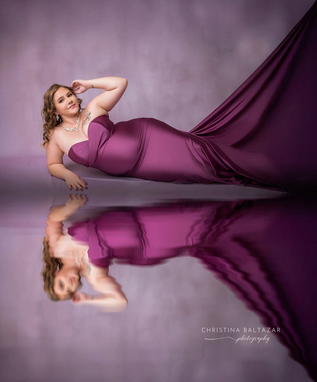 Maternity portrait with flowing burgundy fabric dress and reflection on glossy surface in a studio setting. Hanford Maternity Photographer