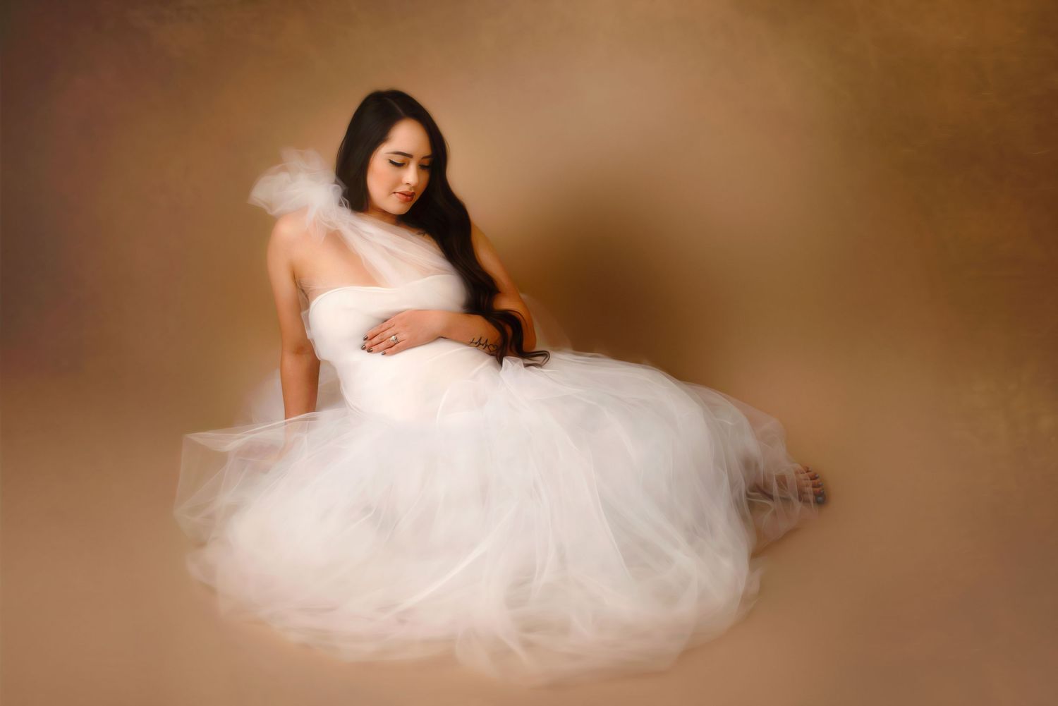 Maternity portrait featuring a white tulle dress against a warm brown studio backdrop creating an ethereal mood. Fresno Maternity Photograph