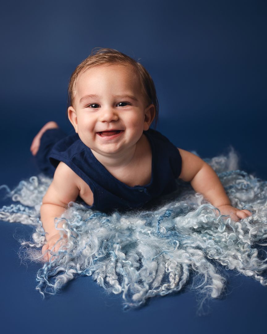 Baby wearing navy outfit lying on white textured fabric with dark blue background.