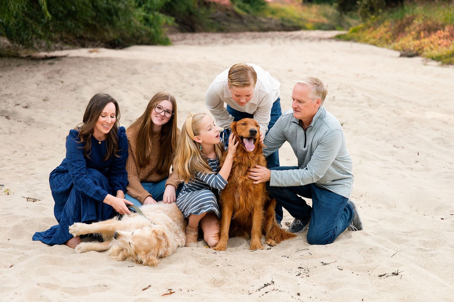 Family and their golden retriever dogs pose together on sandy riverbed. Hanford Family Photographer