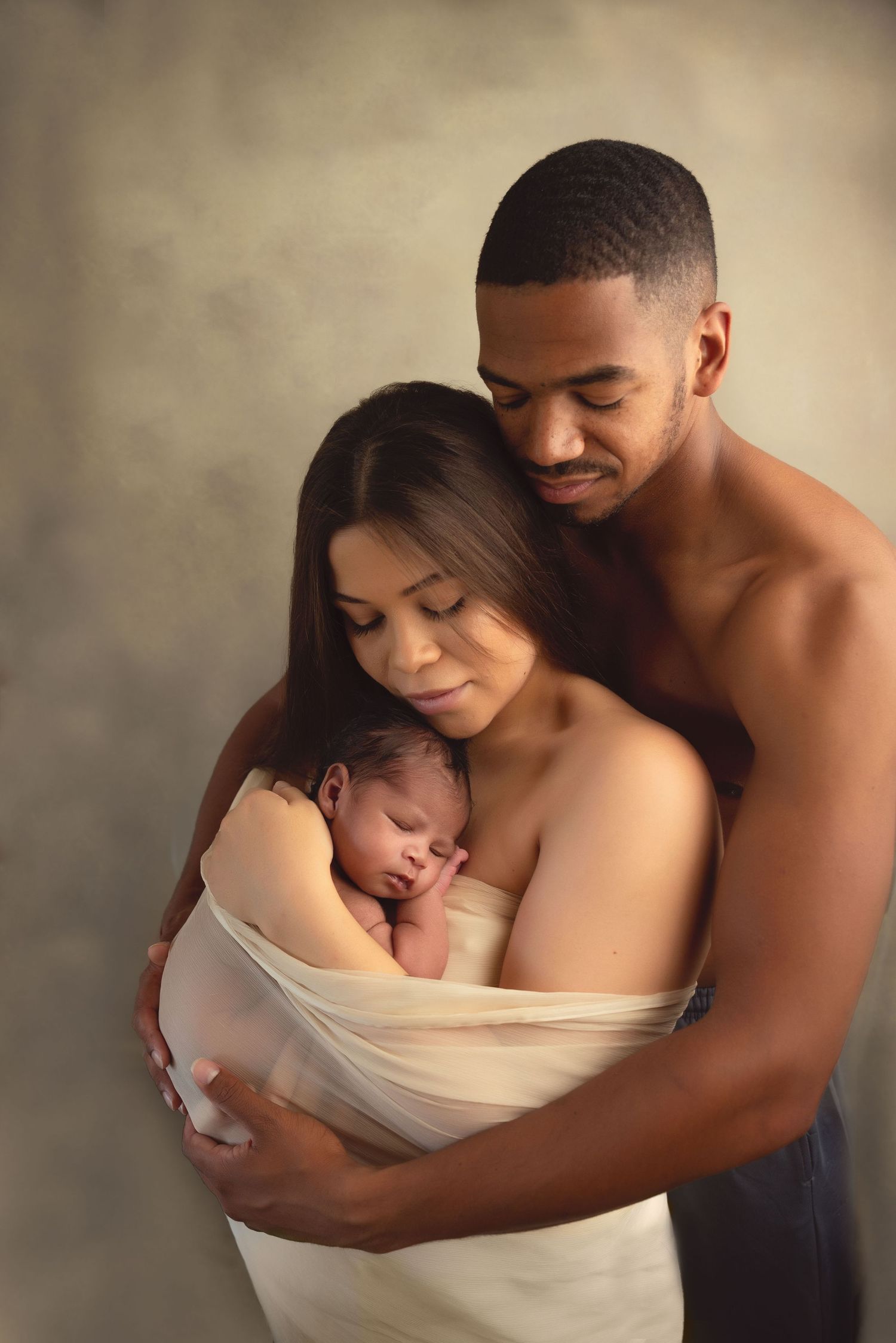 A tender embrace captured in a series of intimate portraits of a father & mother holding their newborn with soft lighting and neutral tones.