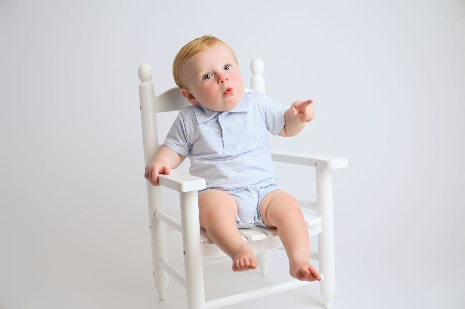 Baby in light blue outfit sitting and playing on white wooden chair. Hanford Baby Photographer