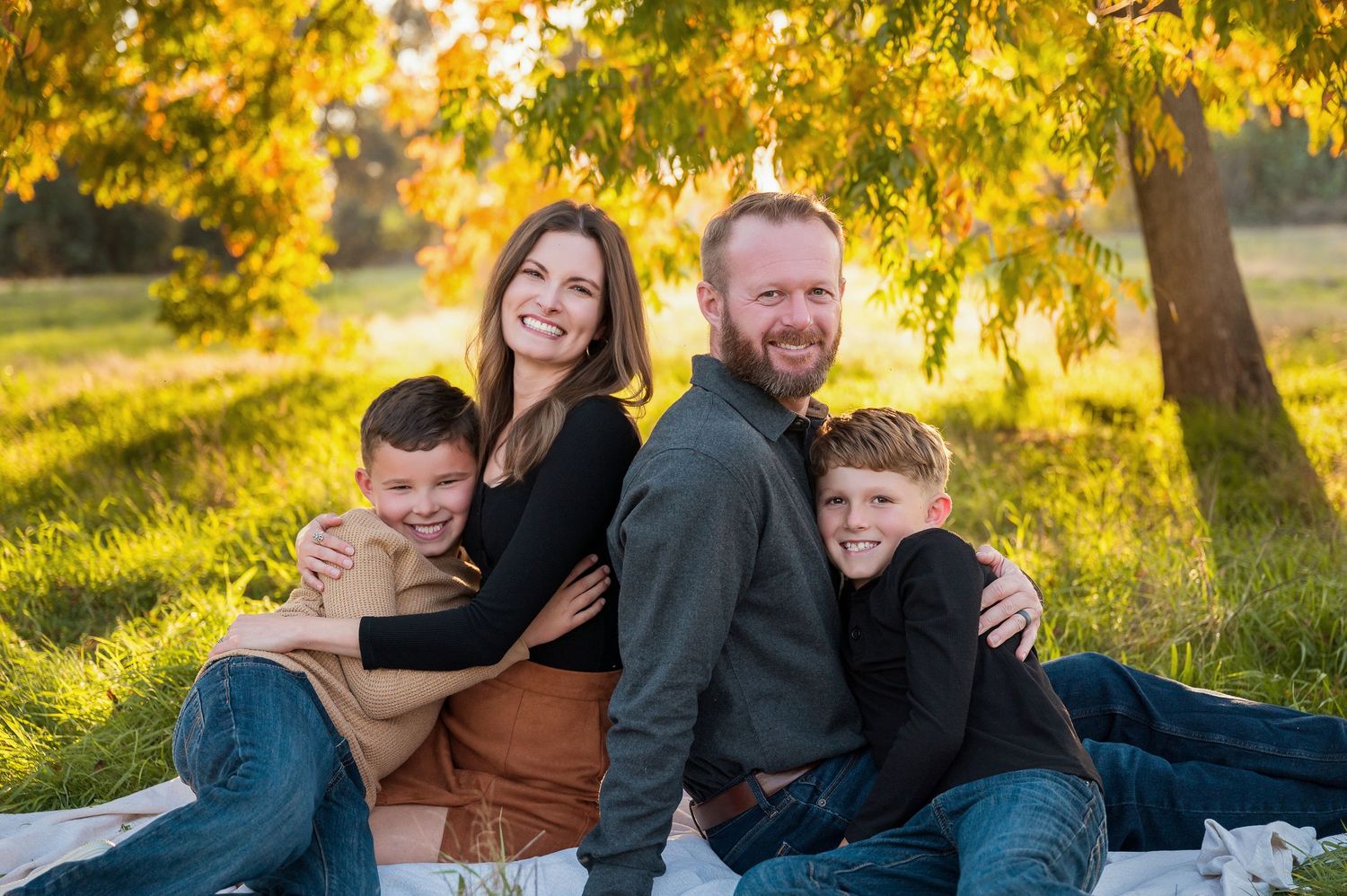 Family relaxes on blanket in grass during golden sunset photo session. Hanford Family Photographer