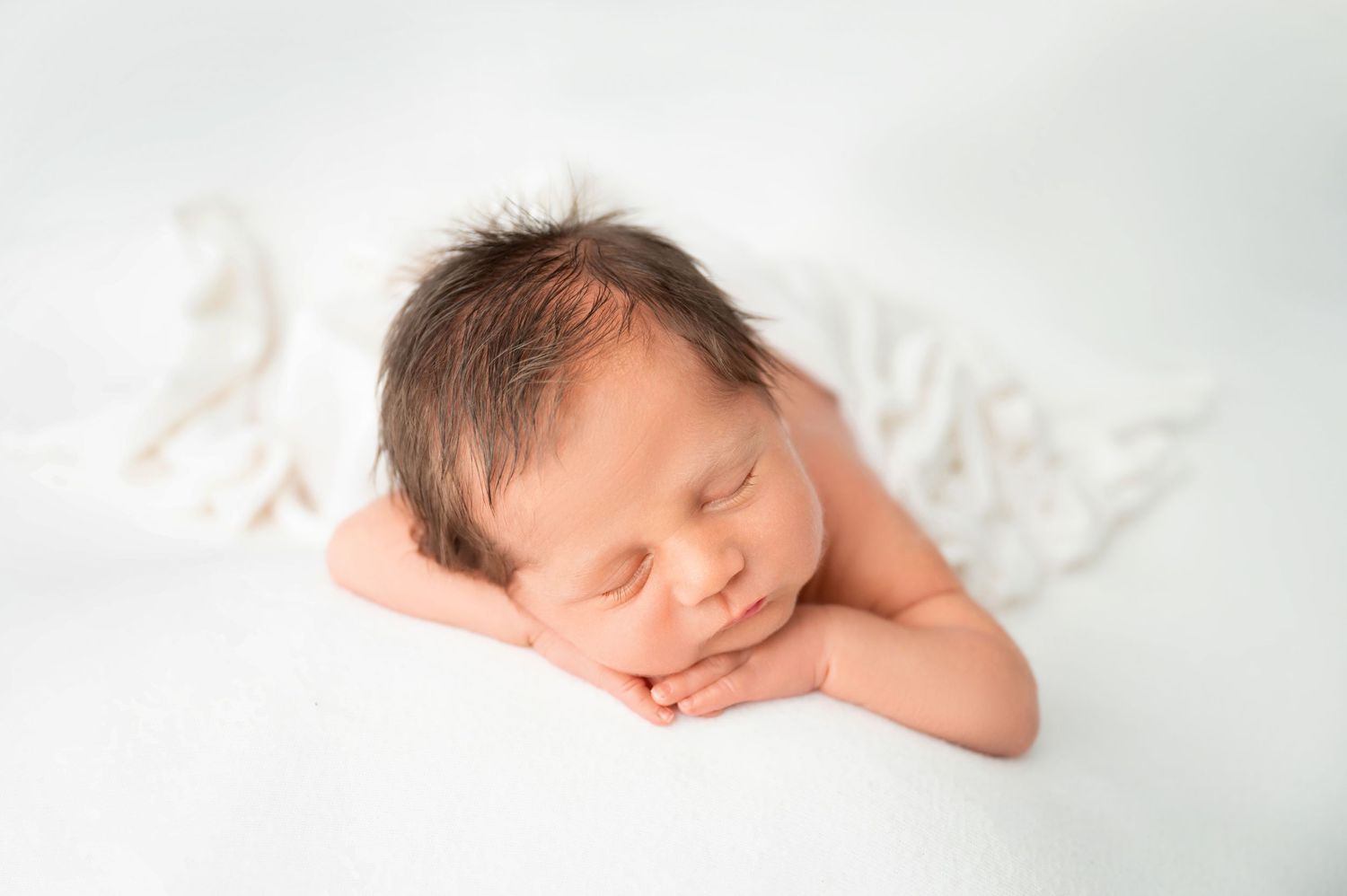 Peaceful sleeping newborn resting on white blanket in artistic portrait.