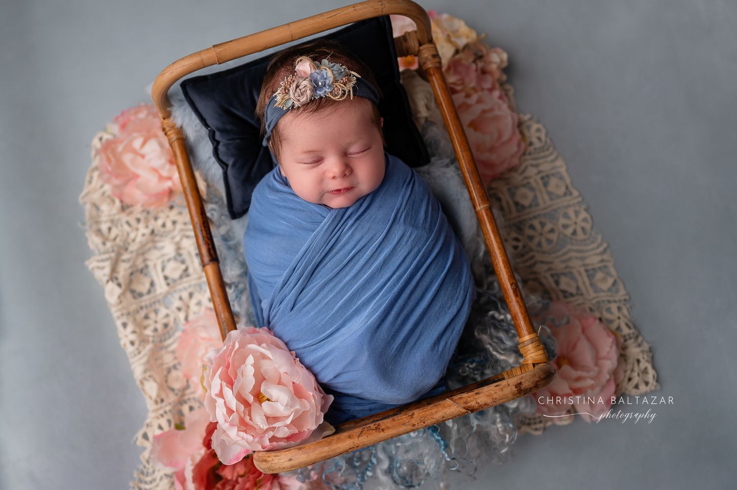 Newborn baby wrapped in soft blue swaddle sleeping peacefully with delicate pink floral accents and crown. Fresno Newborn Photographer