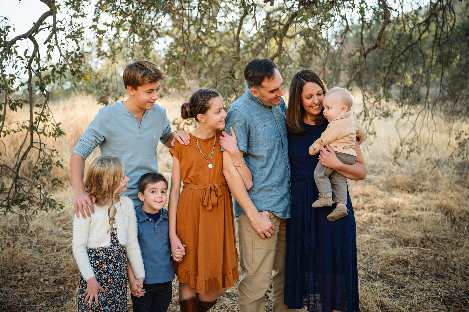 A family wearing coordinated blue and rust colored outfits shares joyful moments during an outdoor photo session.
