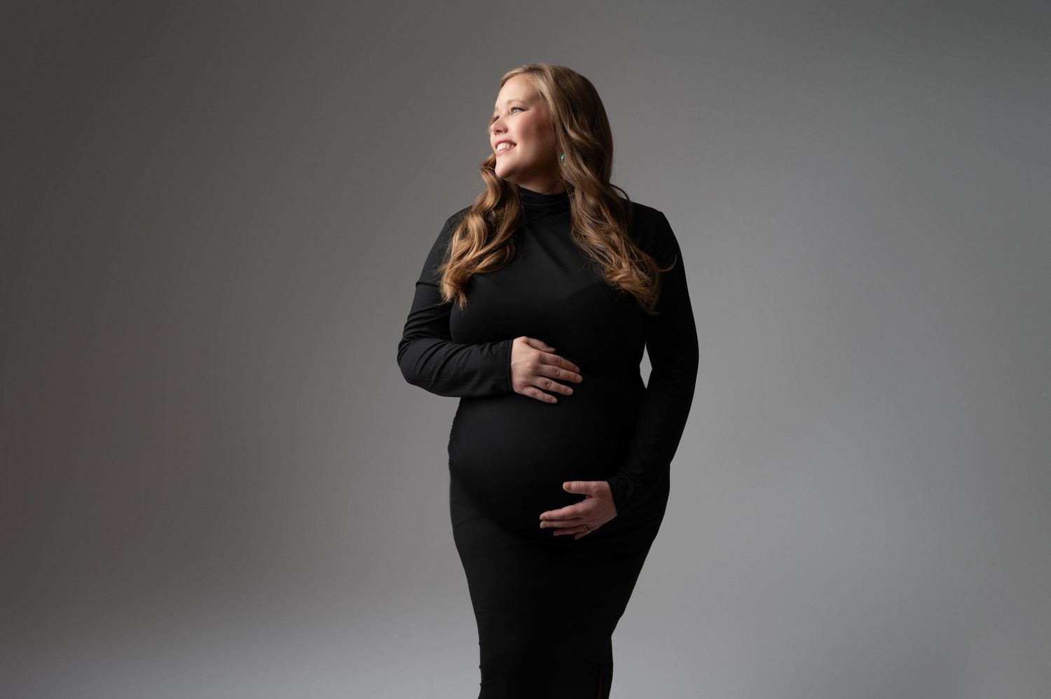 Elegant maternity portraits in black dress against grey studio backdrop.