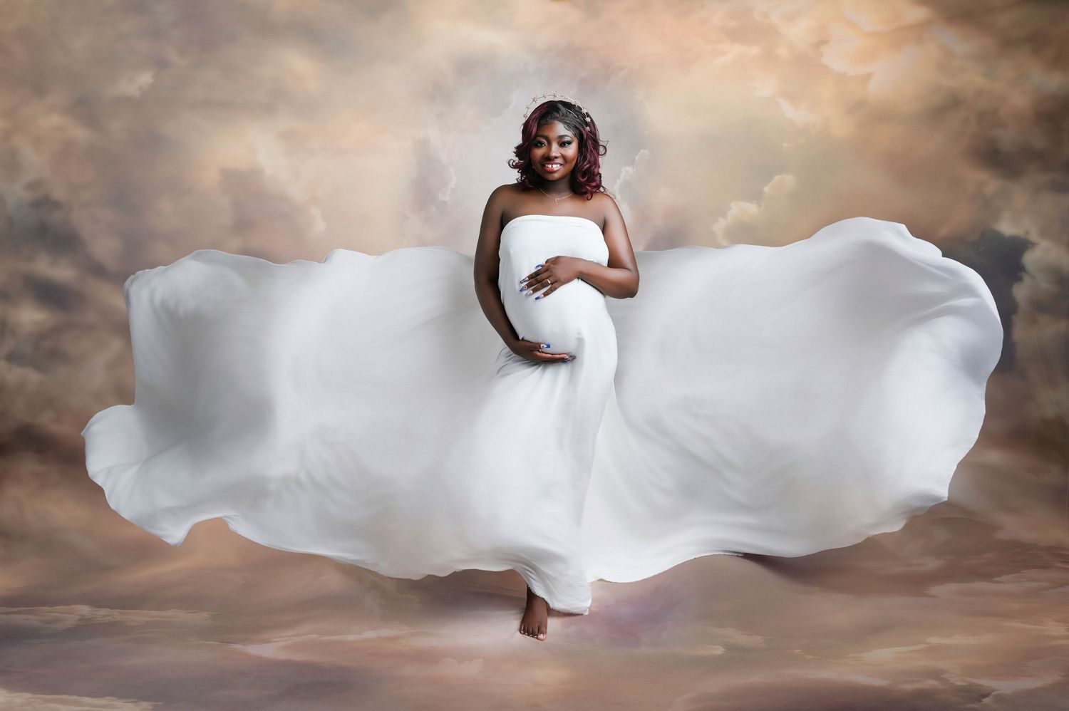 Dynamic maternity portrait with billowing white fabric against dramatic sky backdrop.