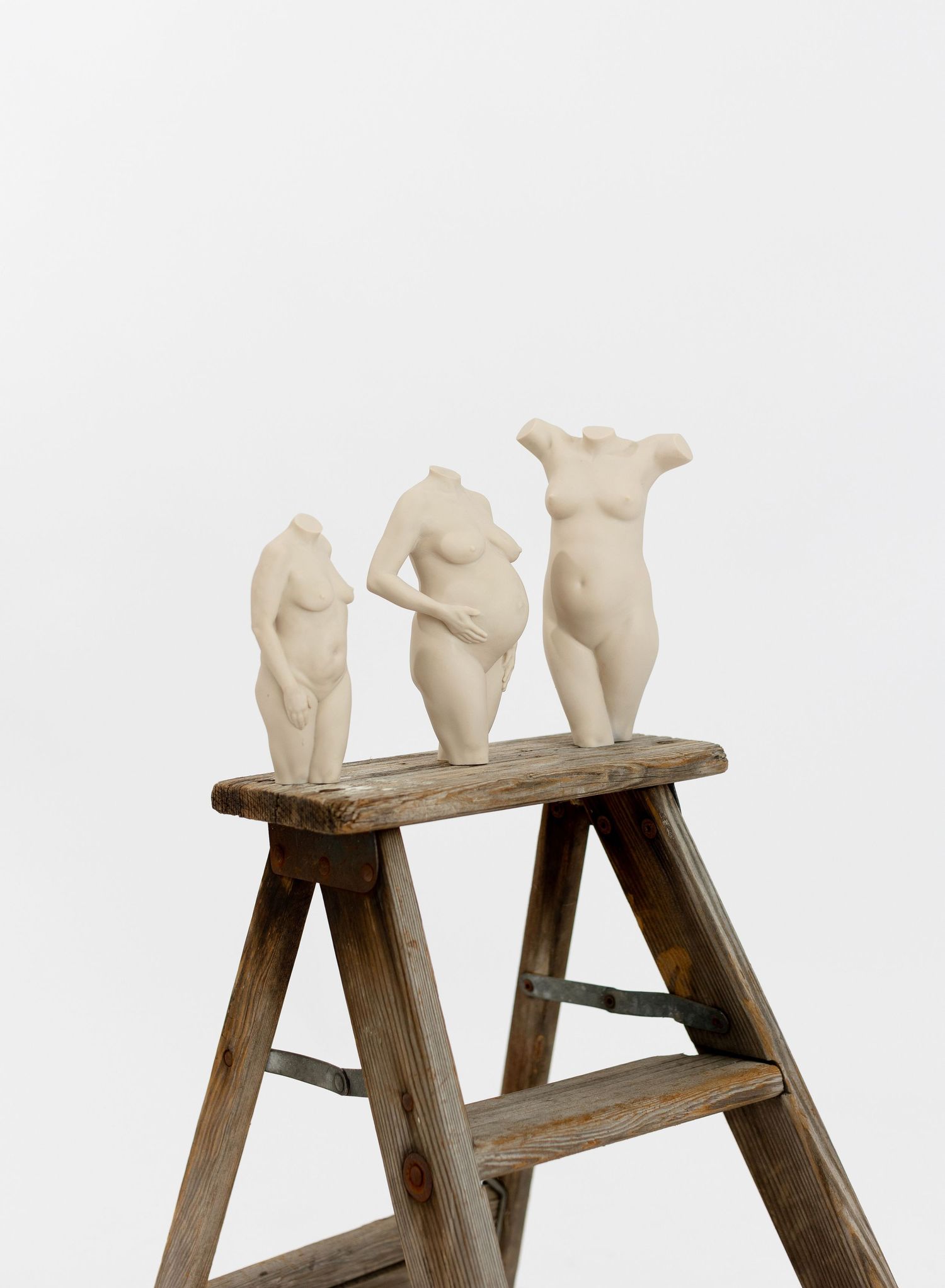 Three small white ceramic pregnancy sculptures displayed on a rustic wooden step ladder against a white background.  3D Pregnancy Sculpture