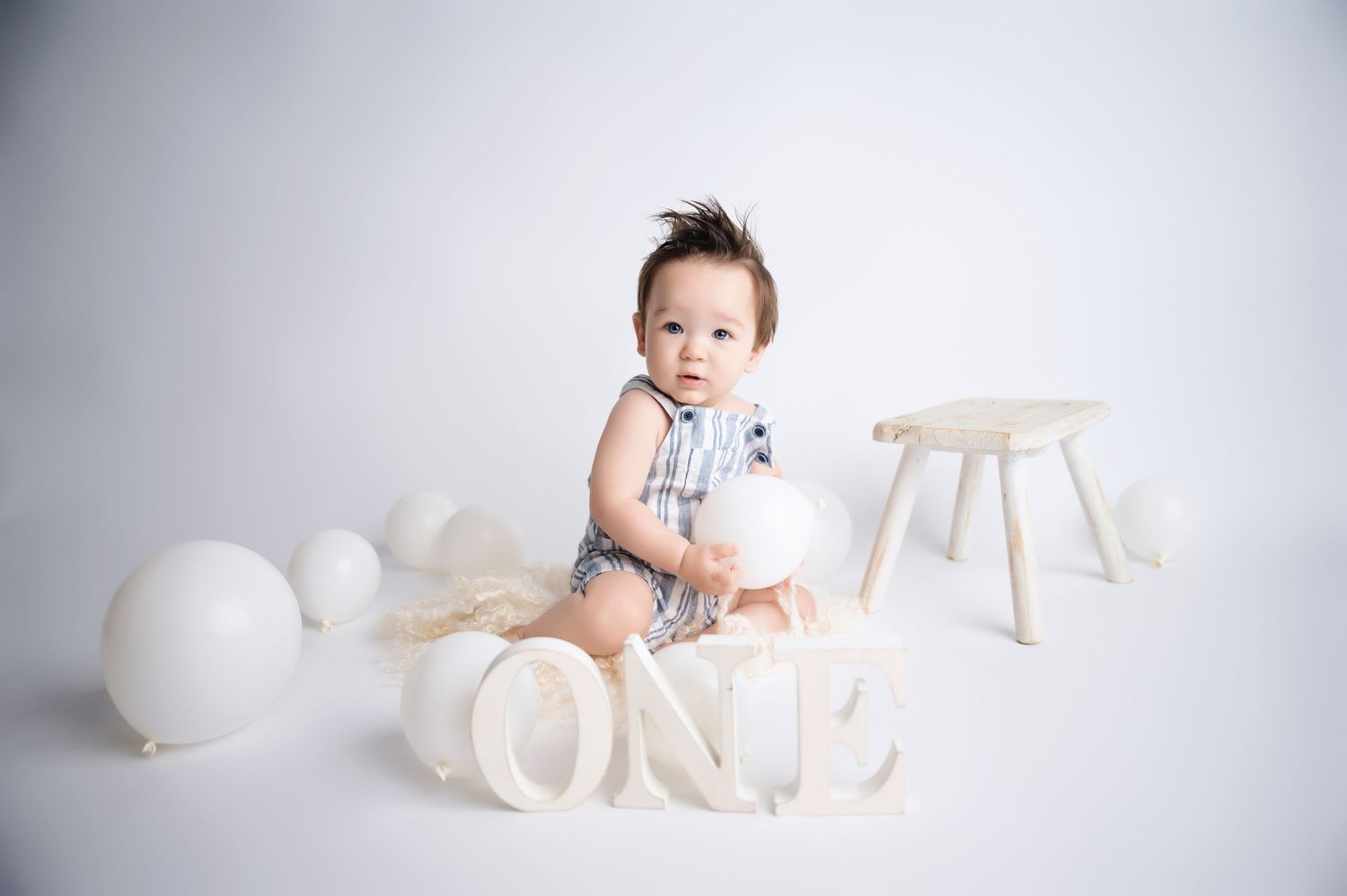 Baby milestone photo session with white balloons and decorative letters against light background.