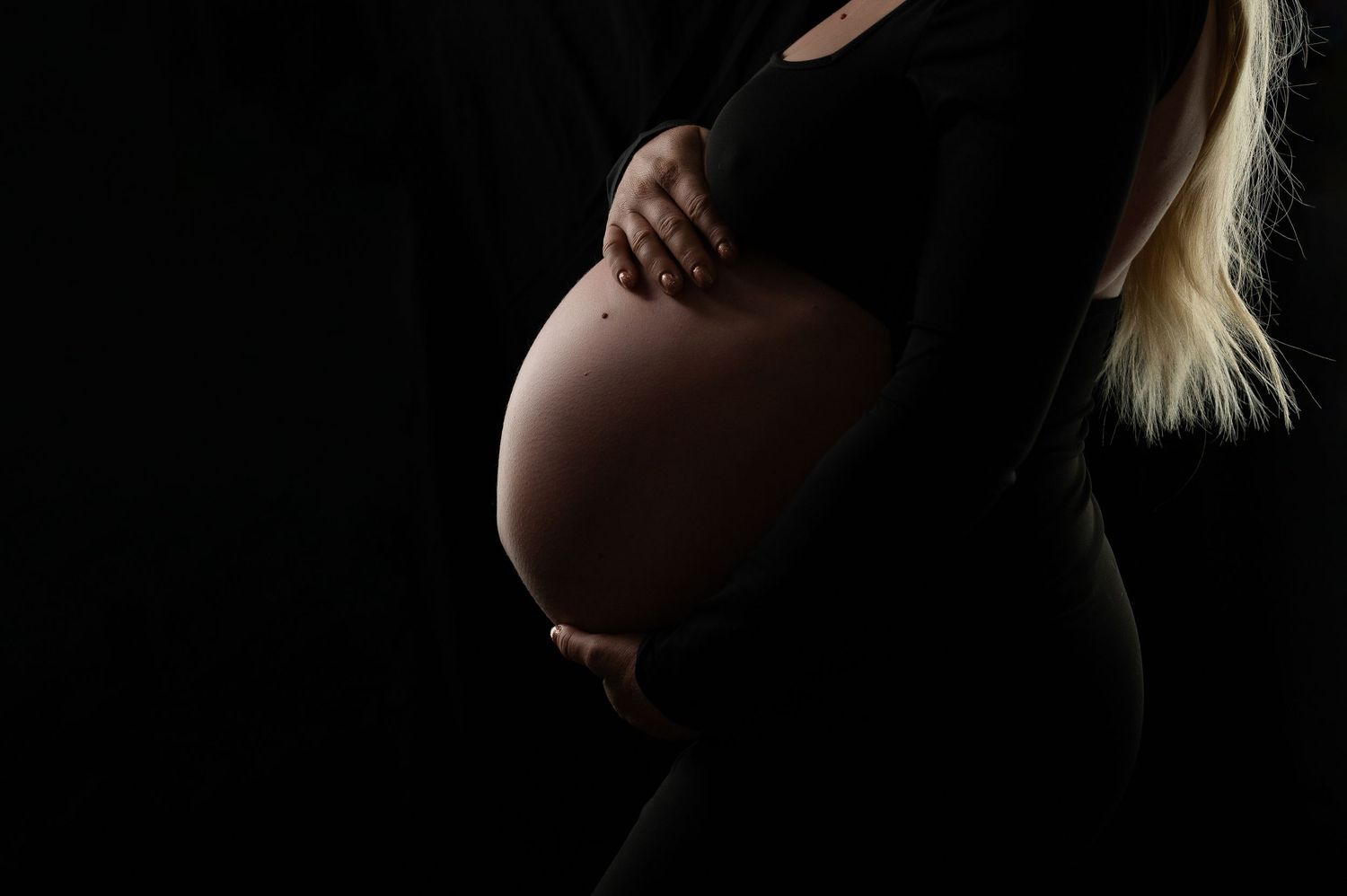 Dramatic silhouette maternity portraits in dark studio setting.