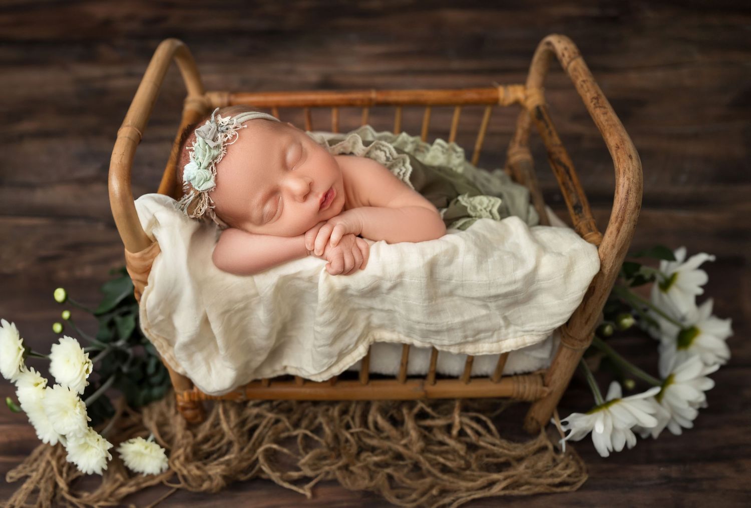 Rustic newborn photography with baby sleeping in wooden basket surrounded by white flowers.